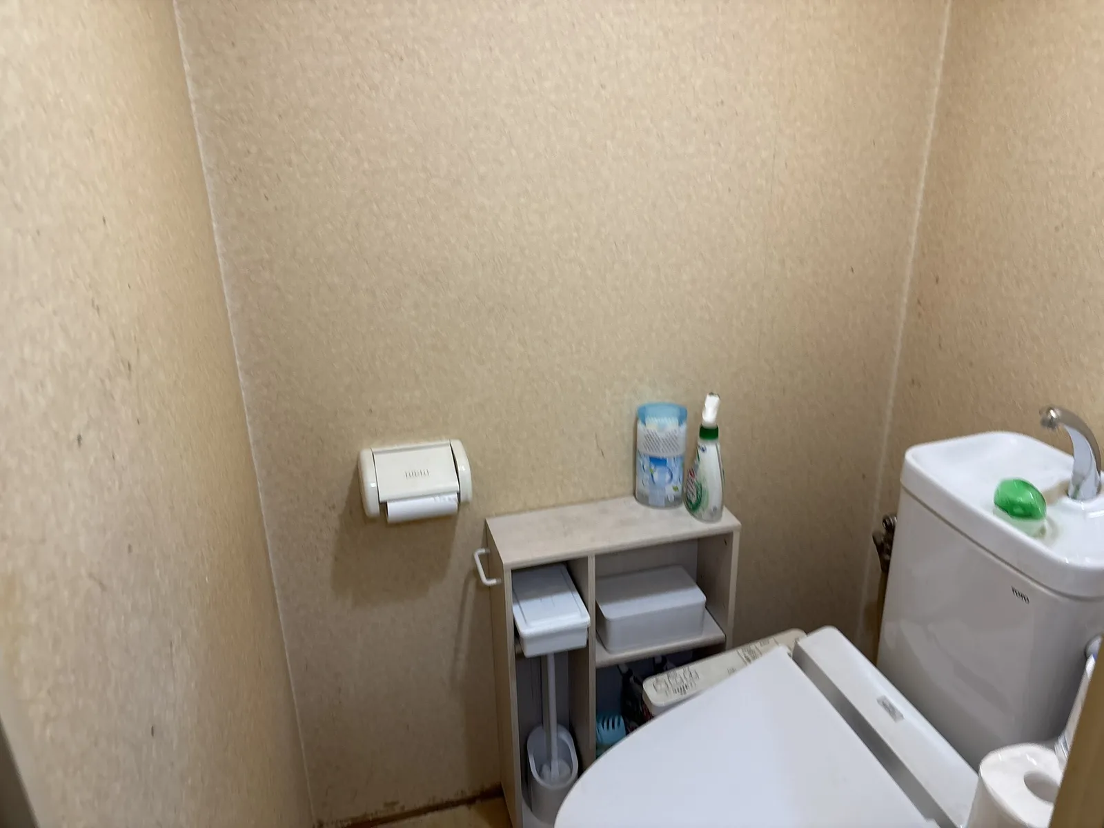 ベージュ系の壁紙に経年による汚れが見られる、リフォーム前のトイレの様子