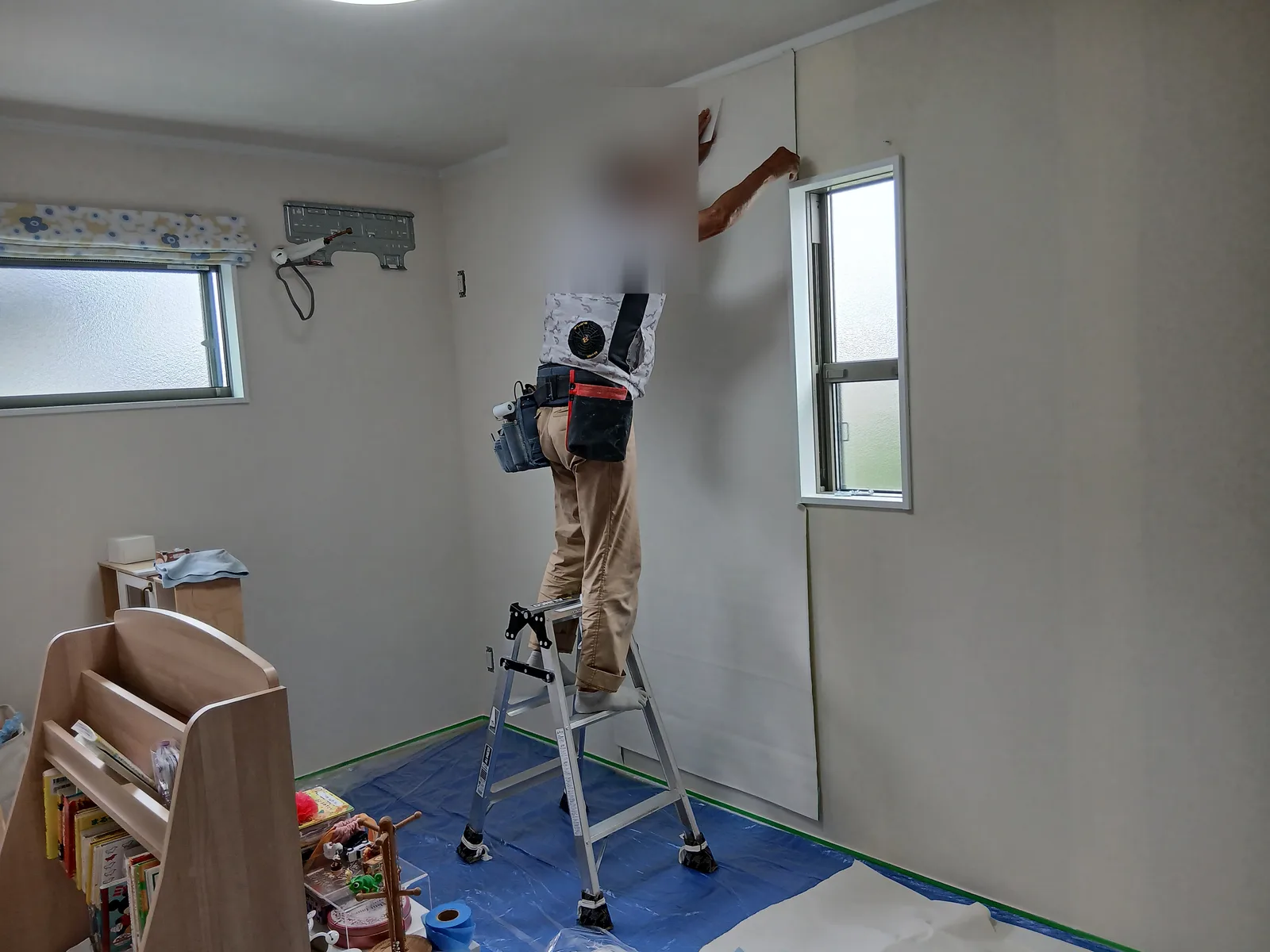縦長の窓のある壁に、職人が新しい壁紙を張っているところ