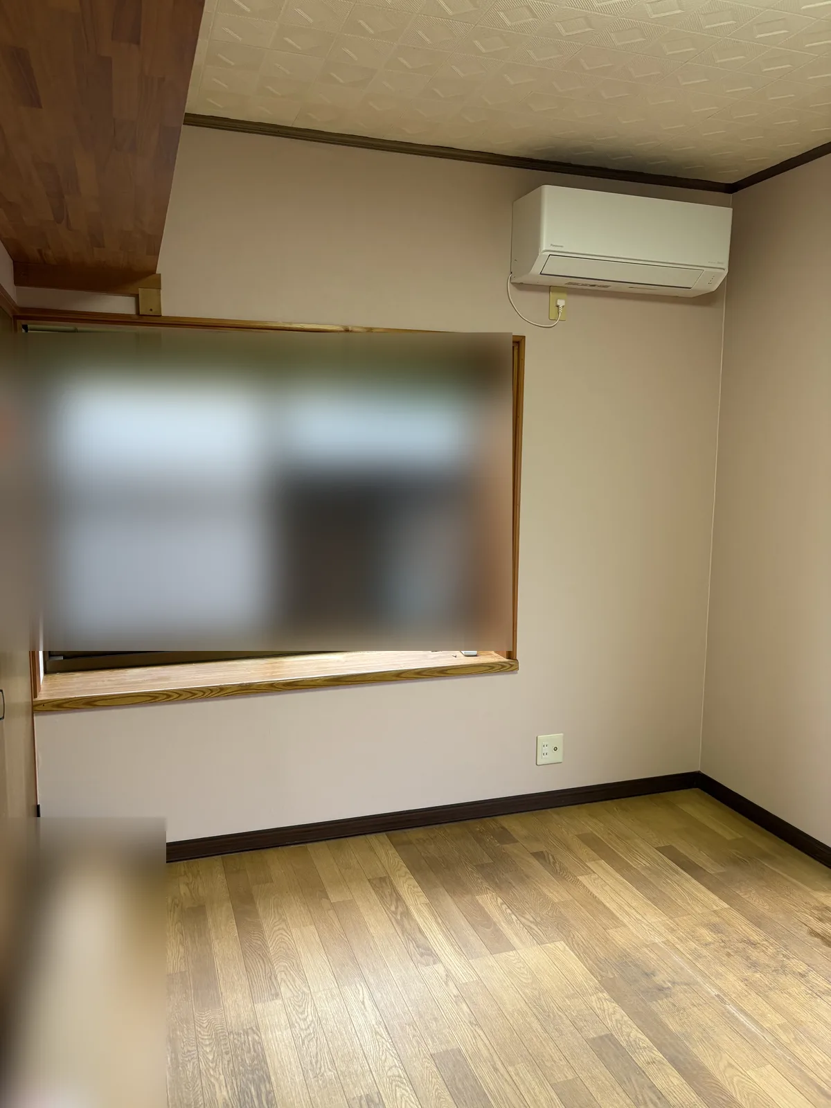 同じエアコンと窓のある壁。淡い色の無地調の壁紙に張り替えた状態