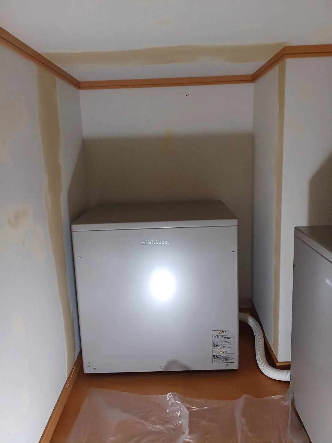 床に置かれた機器のある納戸の奥。壁と天井の際にパテを塗った状態