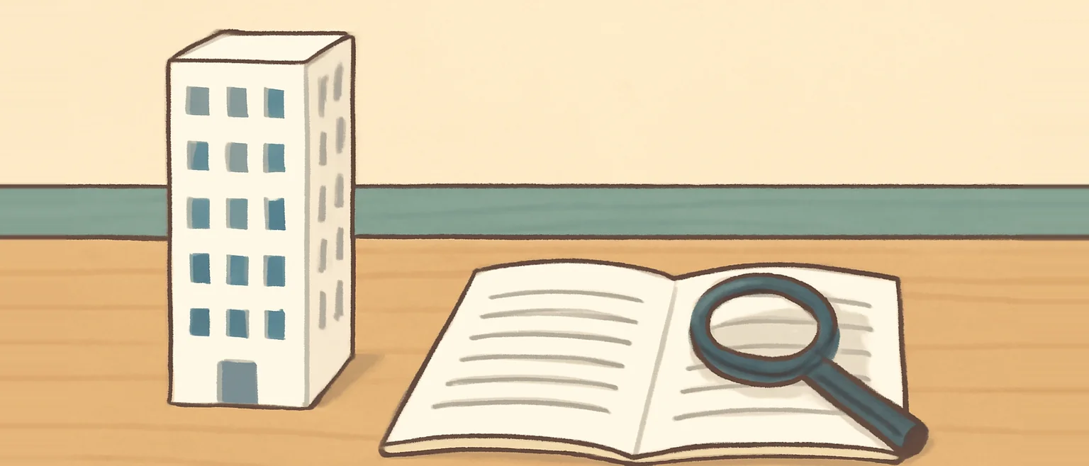 机の上に置いたマンションの模型と、虫眼鏡をのせて開いた冊子