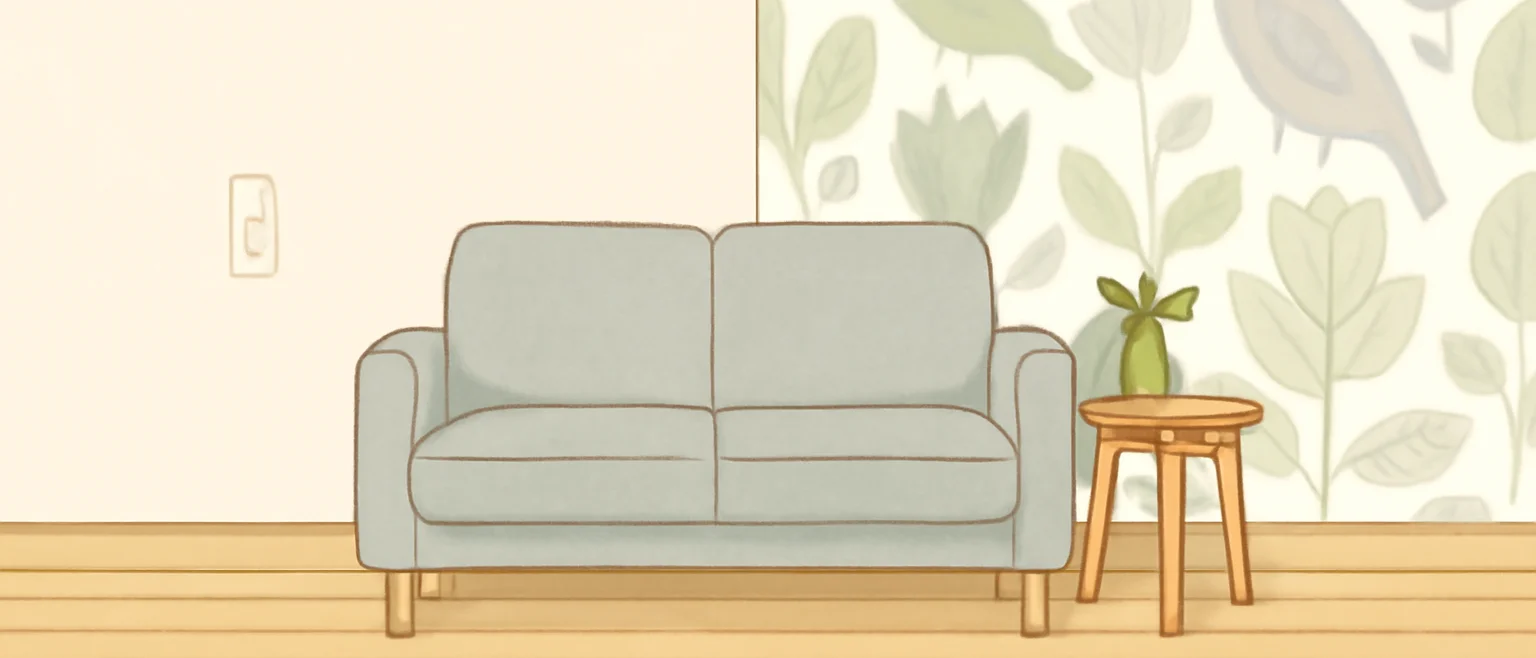 明るいリビングで、無地の壁の隣に植物と鳥の柄の壁紙を1面だけ貼った部屋と、グレーのソファ