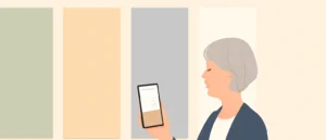 壁に並んだ壁紙の見本パネルの前で、スマートフォンの部屋の写真を見ながら見比べている年配の女性