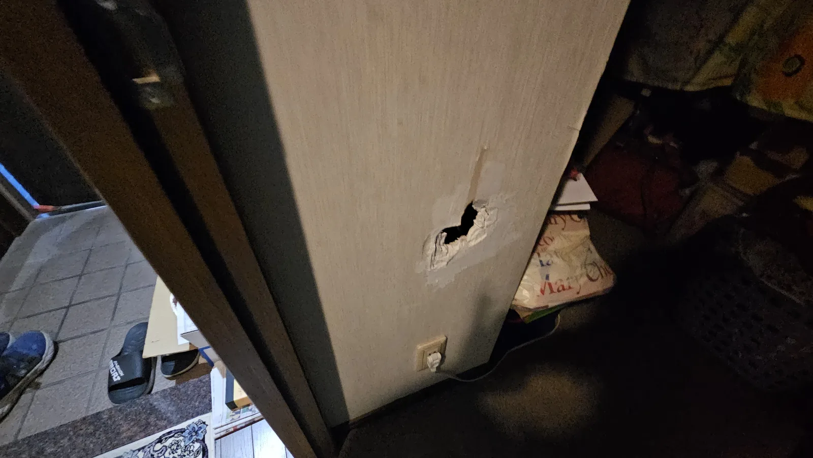 施工前の玄関の近くの壁。コンセントの上に穴が開き、壁紙の下の石膏ボードまで欠けている