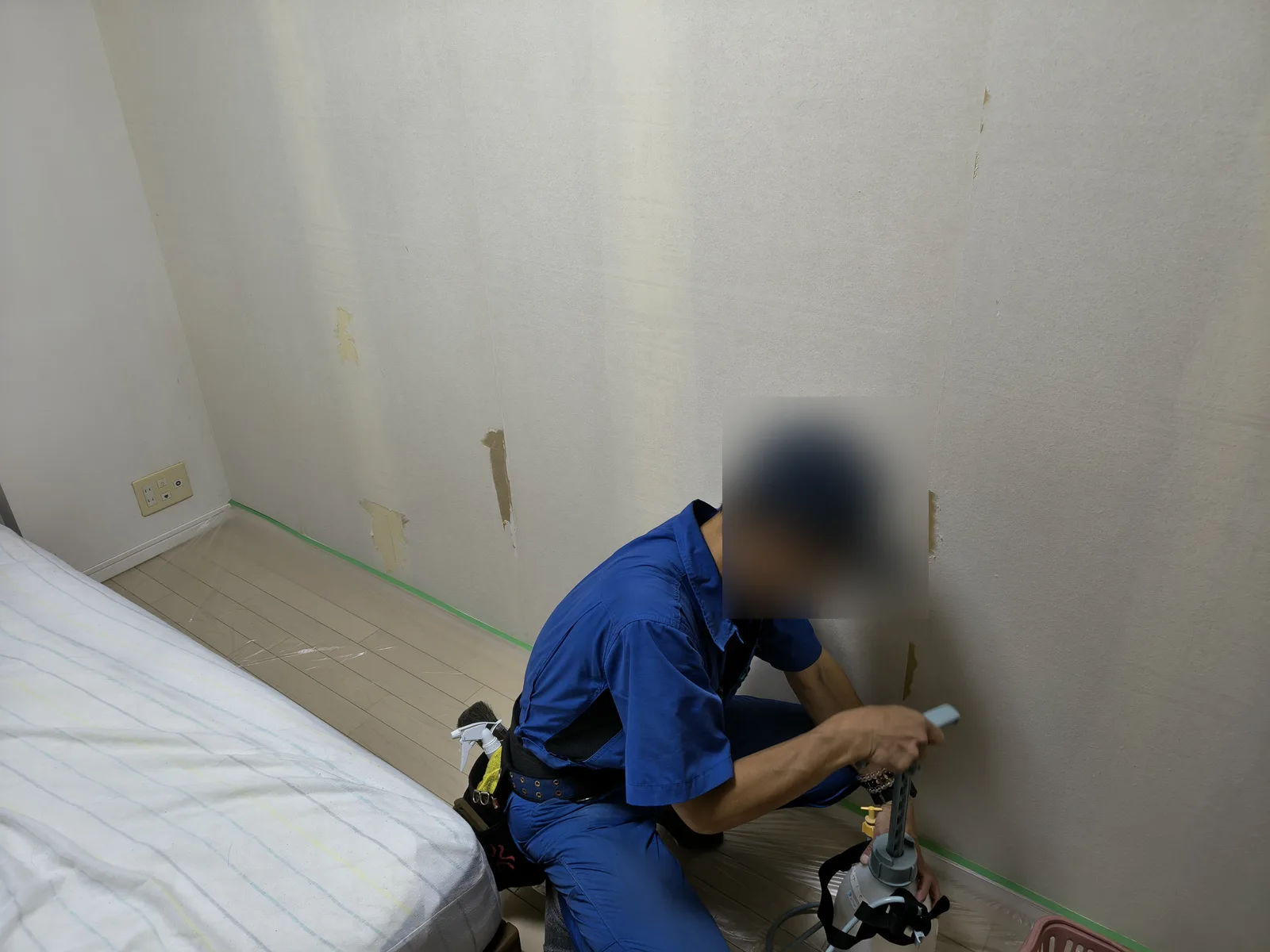 既存の壁紙を剥がした後の壁に、職人が噴霧器で消臭処理をしている様子。床は養生シートで保護している