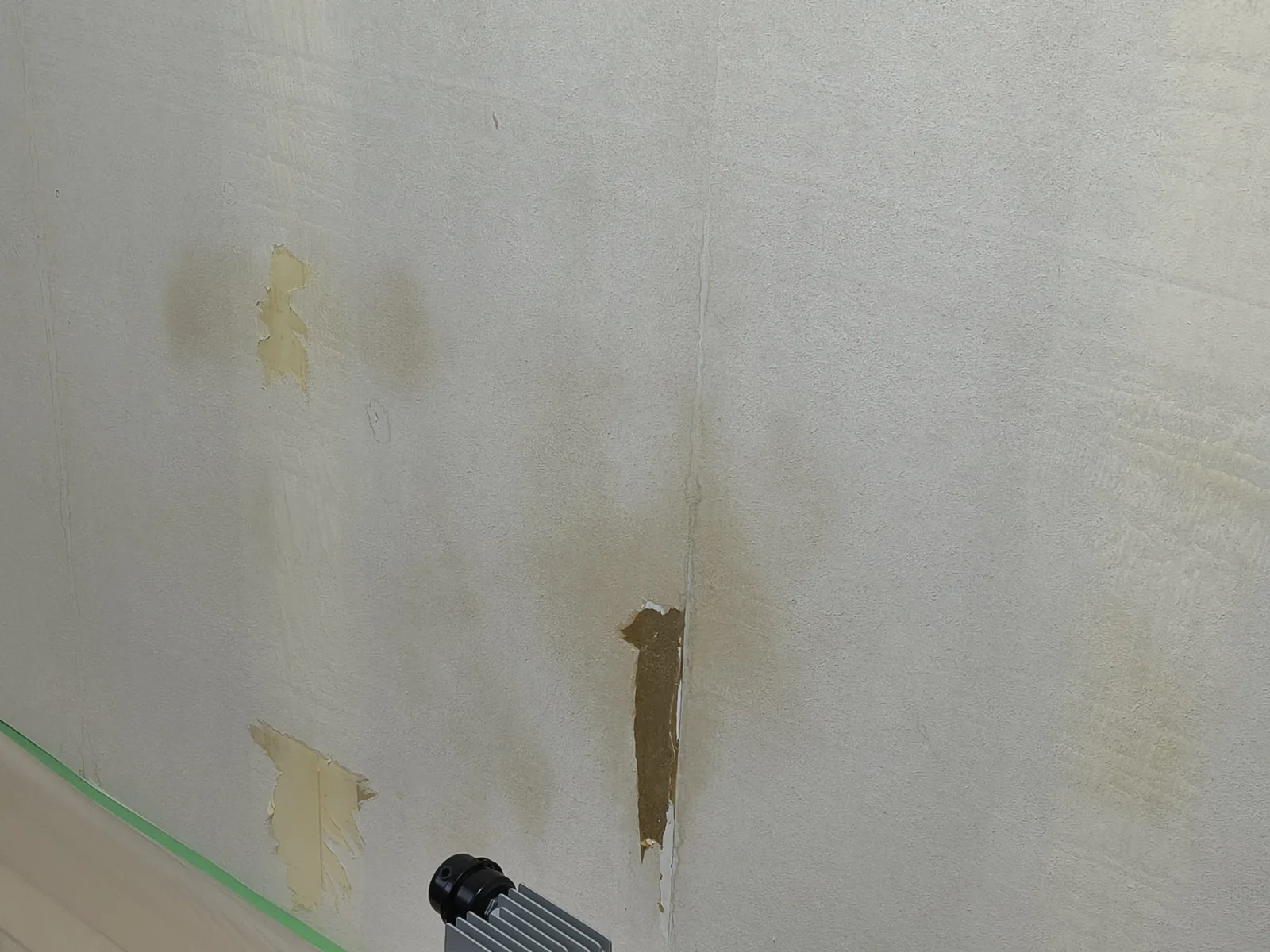 剥がした後の下地のアップ。壁紙の裏紙が残った面に茶色っぽいシミが見え、裏紙が破れて下地がのぞいている箇所もある