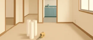家具のない空室の部屋の床に、壁紙のロールとメジャーが置かれている様子